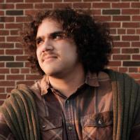 A picture of a guy with curly hair looking over to his left with a brick background